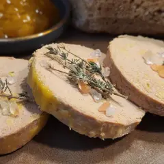 Trzy plastry foie gras, posypane solą i gałązkami tymianku, obok dżemu i chleba. Foie gras co to? Delikatesowy pasztet z gęsiej lub kaczej wątróbki.