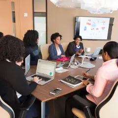 A diverse team collaborates in a meeting room, with one woman acting as an internal coach, guiding the discussion.