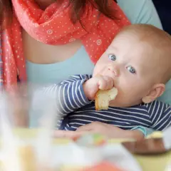 Bambino con occhi azzurri assaggia un pezzo di pane, un momento chiave per capire quando iniziare lo svezzamento.