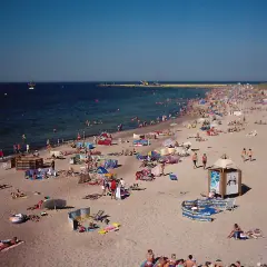 Tłum ludzi wypoczywa na plaży w Darłówku. Słońce, morze i piasek tworzą idealne warunki do relaksu.