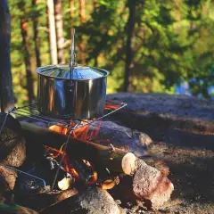Olla de metal sobre una parrilla encima de una fogata, lista para cocinar. Un bushcrafter prepara su comida en la naturaleza.
