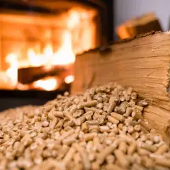 Un tas de granulés de bois devant un poêle à bois crépitant. Une bûche de bois repose sur les granulés, prête à être utilisée.