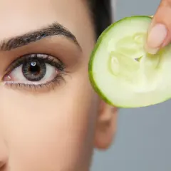 Une tranche de concombre est tenue près de l'œil, une méthode naturelle pour enlever les poches sous les yeux.