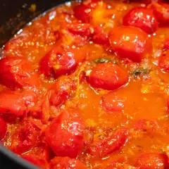 Ein köstlicher, blubbernder Sugo di Pomodoro mit ganzen Kirschtomaten, der in einem Topf köchelt.