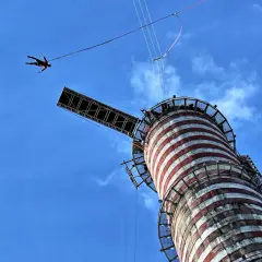Osoba skacze na bungee z wieży, doświadczając adrenaliny. To najwyższe bungee w Polsce, oferujące niezapomniane wrażenia.