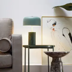 Stylowa lampa metalowa z zielonym kloszem i marmurową podstawą, obok kanapy i obrazu.