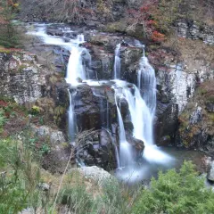 Il sentiero delle cascate serpeggia tra rocce e foliage autunnale, con l'acqua che scende impetuosa.
