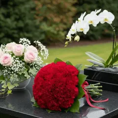 Nowoczesne stroiki na cmentarz: bukiet czerwonych goździków, różowe róże z gipsówką i biała orchidea na czarnym tle.