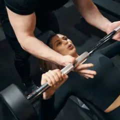 Une femme commence la musculation avec un haltère, guidée par un coach.