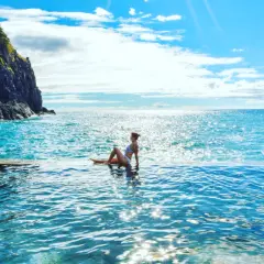 Madera, listopad. Kobieta w basenie infinity z widokiem na ocean. Słoneczna pogoda i błękitne niebo.