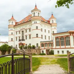 Zamek w Łomnicy, biała budowla z czerwonymi dachami i wieżyczkami, otoczona zielenią.