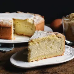 Una fetta di torta di riso, la ricetta originale, cosparsa di zucchero a velo, accanto alla torta intera e a una tazza di riso.