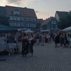 Menschen genießen den Abend auf dem Markt Remscheid. Stände mit Zelten und Tische unter Sonnenschirmen laden zum Verweilen ein.