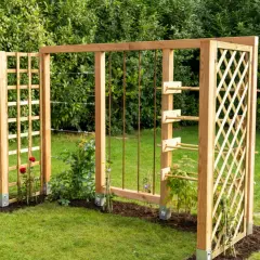 Holzkonstruktion im Garten mit Rankhilfen, die an Baustahlmatten erinnern. Kletterrosen und junge Pflanzen wachsen daran empor.