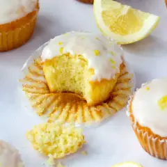 Saftige Zitronen-Magdalenas, eines davon angeknabbert, mit Zuckerguss und Zitronenschale bestreut. Ein perfektes magdalenas rezept für den Nachmittagstee.