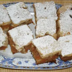 Na talerzu ułożono porcję 10 najlepszych ciast z jabłkami, posypanych cukrem pudrem.