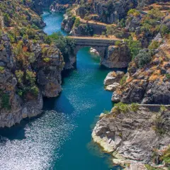 Cañón con río azul y puente de piedra, evocando la belleza natural de los pueblos de Madrid.