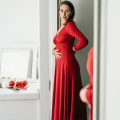 Kobieta w czerwonej, eleganckiej sukience, która optycznie wyszczupla. Na toaletce świąteczne ozdoby i kosmetyki.