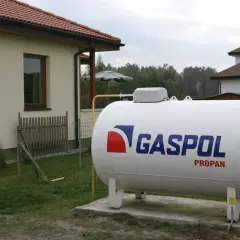 Duży, biały zbiornik z napisem GASPOL PROPAN, stojący obok domu. To jest propan, paliwo do ogrzewania.