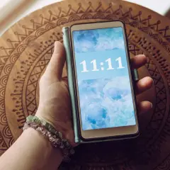 Dłoń z bransoletkami trzyma telefon z wyświetloną godziną 11:11. To znak, że 11.11 znaczenie ma dla wielu osób.