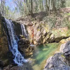 Cascata nella riserva naturale Alto Merse, con rocce colorate e acqua cristallina che forma una pozza verde smeraldo.