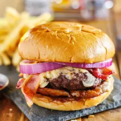 Soczysty burger z bekonem, serem i czerwoną cebulą, podany z frytkami i ketchupem.