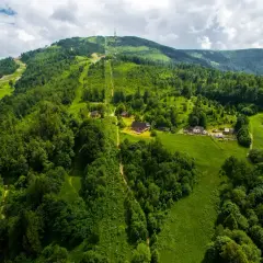 Widok z lotu ptaka na zielone zbocza Skrzycznego, z widocznymi trasami narciarskimi i szlakami pieszymi, domkami i kolejką linową.