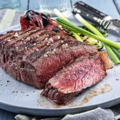 Un pavé de rumsteak grillé, coupé en tranches, servi avec des légumes rôtis et des oignons verts.
