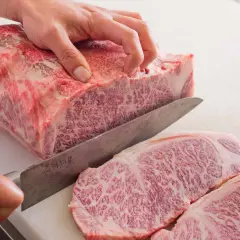 Ręka kroi luksusowe mięso wagyu na desce. Widoczne marmurkowe przerosty tłuszczu świadczą o jego wyjątkowej jakości.