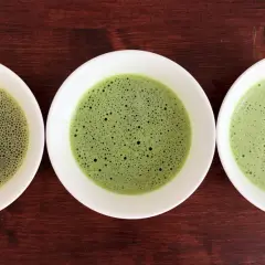 Drei Schalen mit schaumigem Matcha in verschiedenen Grüntönen, von hellgrün bis tiefgrün.