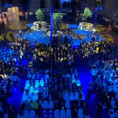 Vue aérienne d'une foule assise dans une **arena Paris** illuminée de bleu, avec des motifs jaunes au sol.