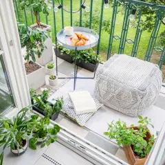 Gemütliche Balkon Ideen: Pflanzen, Kissen, Hocker und ein Tablett mit Croissants laden zum Verweilen ein.