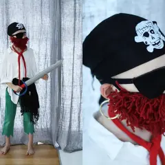 Dziecko w stroju pirata 122: czarna bandama z czaszką, opaska na oko, czerwona broda z włóczki, biała koszula, zielone spodnie i miecz.