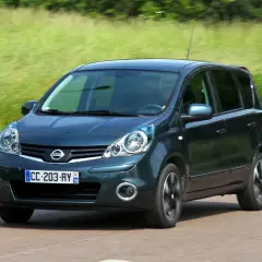 Ciemnozielony Nissan Note E11 w ruchu, z rozmytym tłem zieleni i drogi.