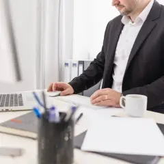 Biznesmen przy biurku, pracujący przy laptopie i klawiaturze. Może to być związane z wpłatą gotówki na konto firmowe.