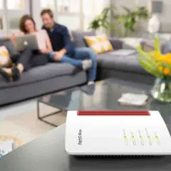 Biały router FRITZ!Box na stoliku, z parą relaksującą się na kanapie w tle. To urządzenie zapewnia domowe Wi-Fi.