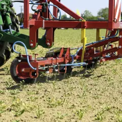 Un tracteur vert et un pulvérisateur rouge travaillent dans un champ de jeunes pousses. La machine applique un traitement ciblé, peut-être pour une liste de graminées à éradiquer.