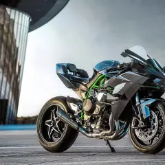 Czarny Kawasaki Ninja H2R, znany jako najszybszy motor na świecie, z zielonymi akcentami, stoi przed nowoczesnym budynkiem.
