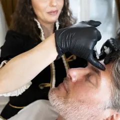 Man ligger ner och får botox i pannan av en kvinna i svarta handskar.