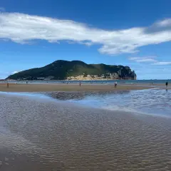 Amplia **playa Laredo** con gente paseando y jugando, bajo un cielo azul con nubes blancas y una gran montaña verde al fondo.