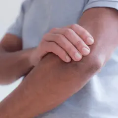 Mężczyzna trzyma się za łokieć, odczuwając ból. Zastanawia się, ile zwolnienia na łokieć tenisisty mu przysługuje.