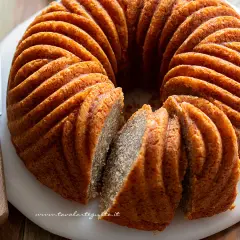 Una torta cachi e mele dorata, con un bordo scanalato, è affettata su un tagliere bianco. Un coltello con manico in legno è appoggiato accanto.