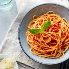 Spaghetti z sosem pomidorowym i bazylią w misce, obok starty ser i sztućce.