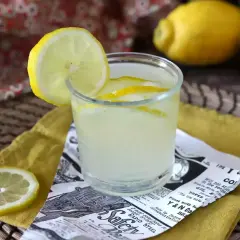 Orzeźwiający drink z limoncello, ozdobiony plasterkiem cytryny, na tle cytryn i wzorzystej tkaniny.