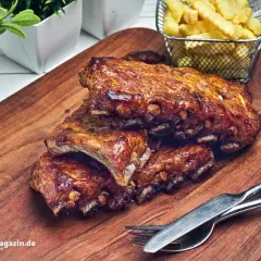 Saftige Spare Ribs, perfekt gegrillt, liegen auf einem Holzbrett. Dazu gibt es knusprige Pommes. Ein tolles spare ribs rezept!