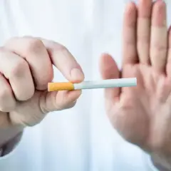 Dłoń trzyma papierosa, druga dłoń pokazuje znak stop. To symbol redukcji szkód i wyboru zdrowszego życia.