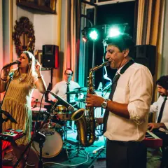 Una band suona musica dal vivo per un matrimonio. La cantante è in primo piano, mentre un sassofonista, un batterista e un tastierista completano il gruppo.