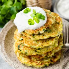 Pile de beignets de courgettes à l'italienne, garnis d'une cuillère de crème et de coriandre fraîche. Un délice croustillant et savoureux.