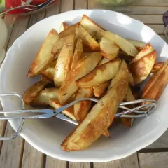 En skål med gyllene klyftpotatis i ugn, redo att serveras med tång.