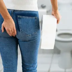 Femme tenant du papier toilette, main sur la fesse, suggérant l'incontinence anale. Recherche d'un traitement naturel.